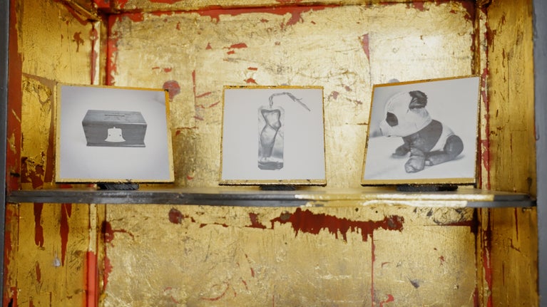 Three sketches in frames set out on a shelf with a gold background